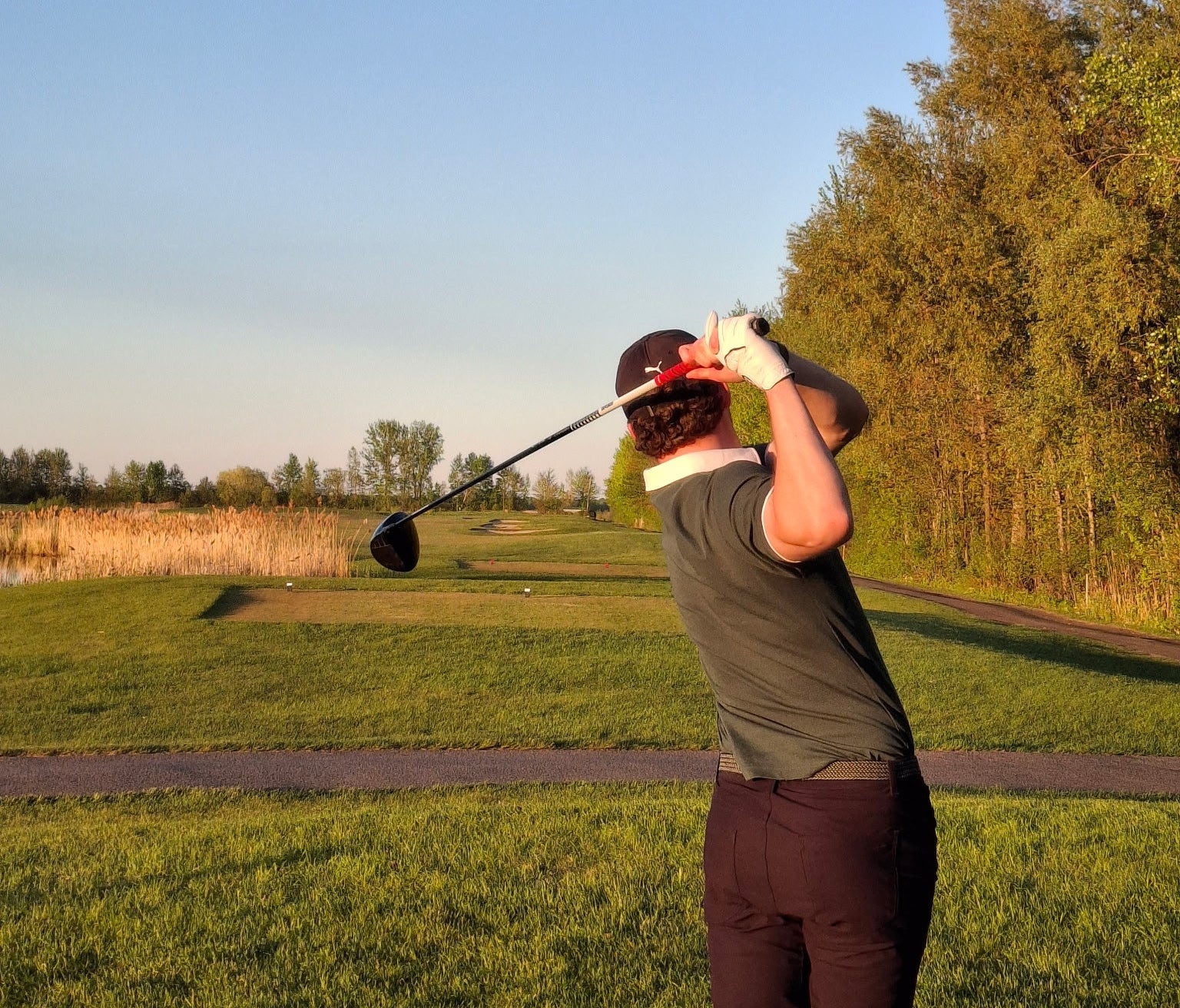 Person playing golf on a grassy course with trees and clear sky in the background